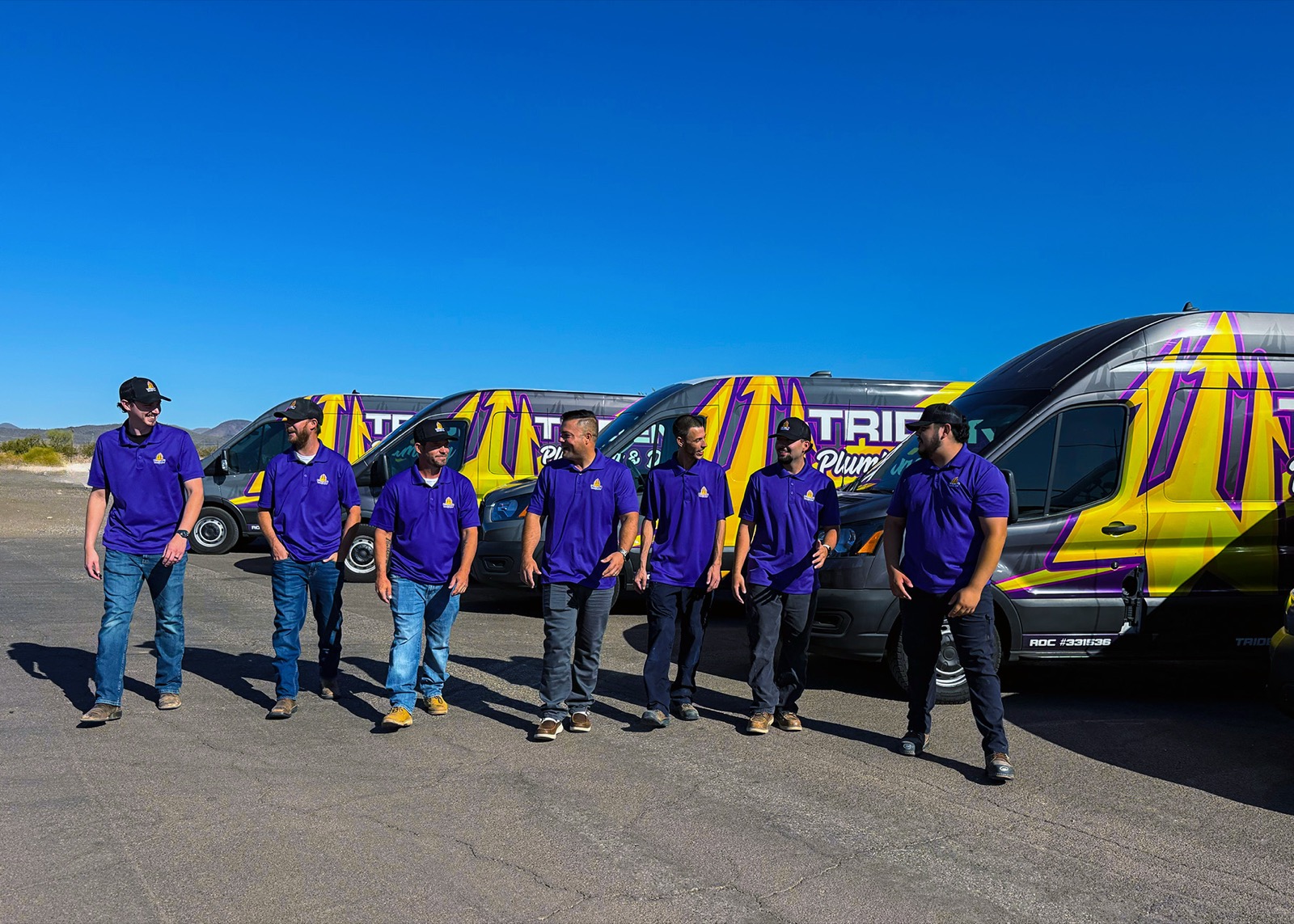 The Trident Plumbing & Drain team walking together with the company fleet behind them.